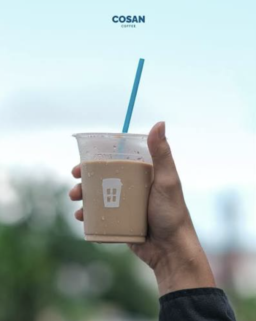 A cup of iced Cosan coffee held against a bright blue sky